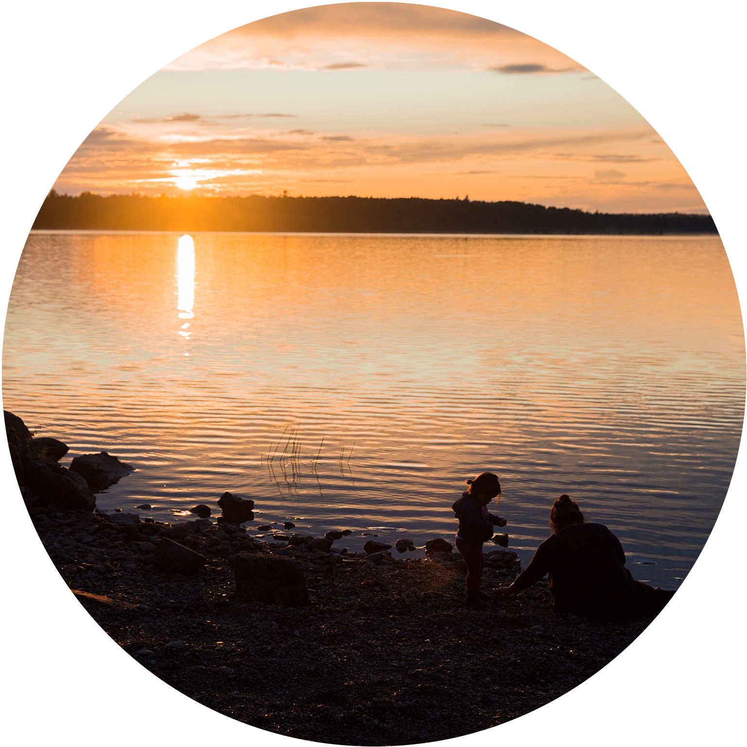 Silhouette of child and parent playing at waters edge at sunset