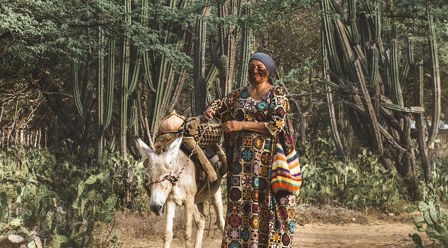 A women with face paintings stands on a dirt road with a donkey