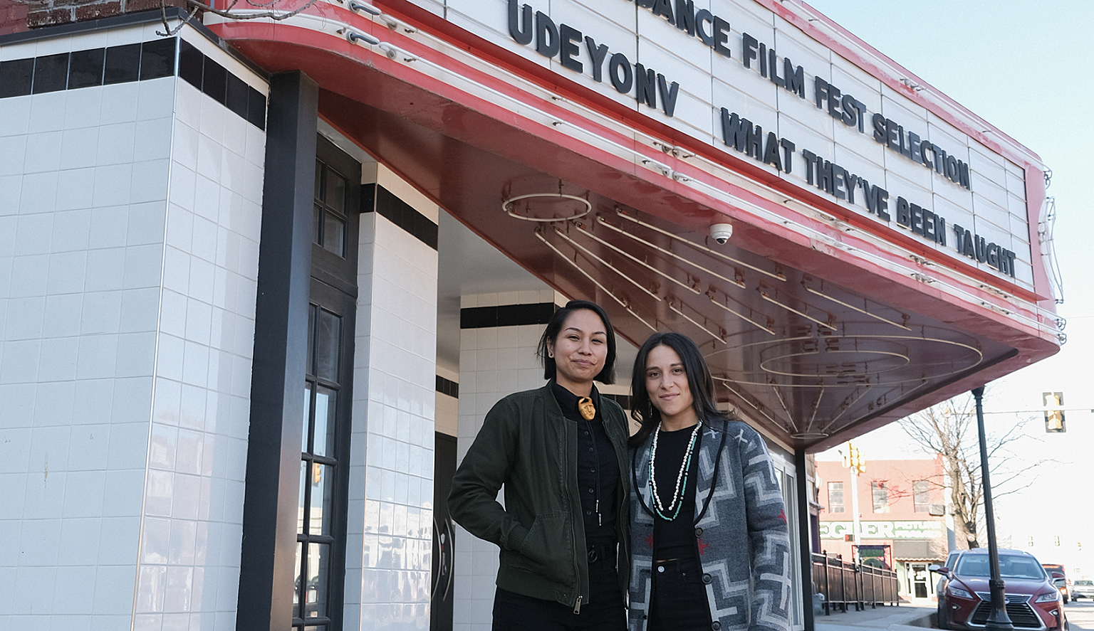 Two people stand in front of a movie marquee