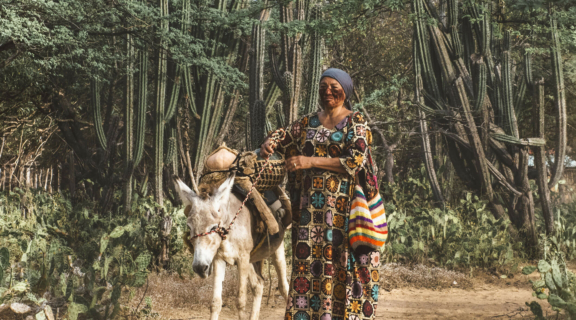 A women with face paintings stands on a dirt road with a donkey