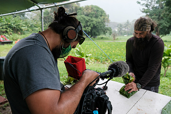 A cameraman records a man folding a large leaf into a package