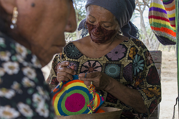A women with dark facial paint across her mouth weaves a bright round basket