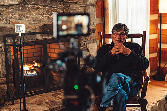 A man sits next to a fireplace being interviewed