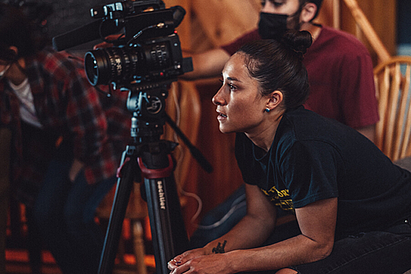 A women leans forward in her seat next to a camera and tripod