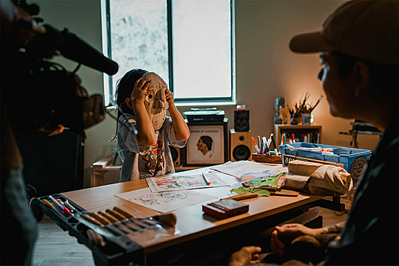 A child is filmed while they cover their face with a wooden mask
