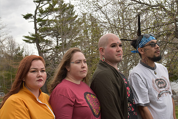 A group of four people look out into the distance while standing in front of a forest of trees