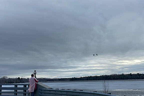 A person in a pink long vest stands at the edge of bridge holding a camera