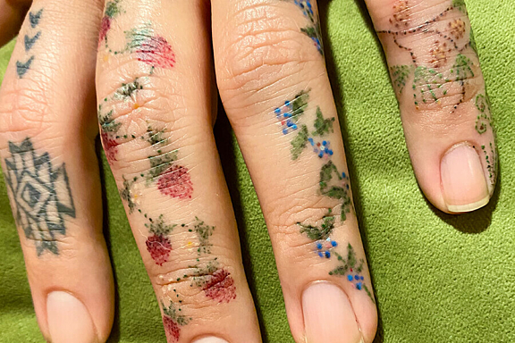 A close up photo of a persons hands with small flower and fruit tattoos