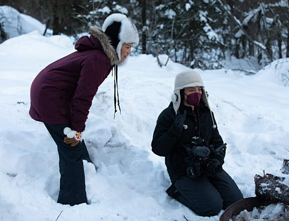 People sitting and standing in snow near a fire