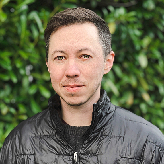 Portrait of a man in a black jacket standing in front of greenery