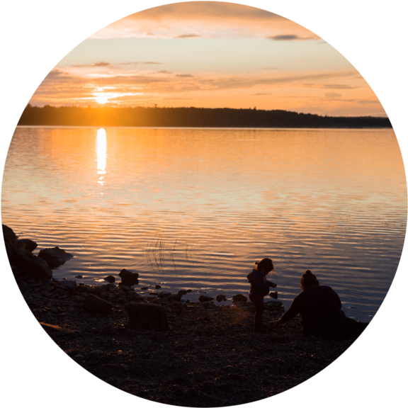 Silhouette of child and parent playing at waters edge at sunset