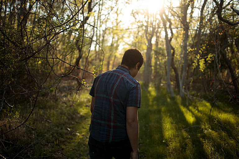 Profile outline of a man standing in a forest with sun shinning down