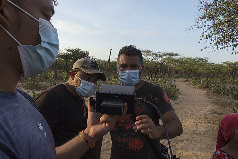 Two men in face masks look at a small portable screen held by third man