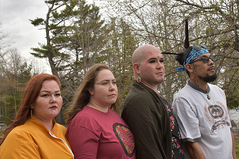 A group of four people look out into the distance while standing in front of a forest of trees