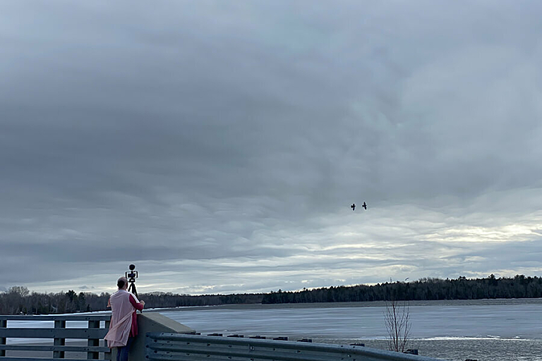 A person in a pink long vest stands at the edge of bridge holding a camera