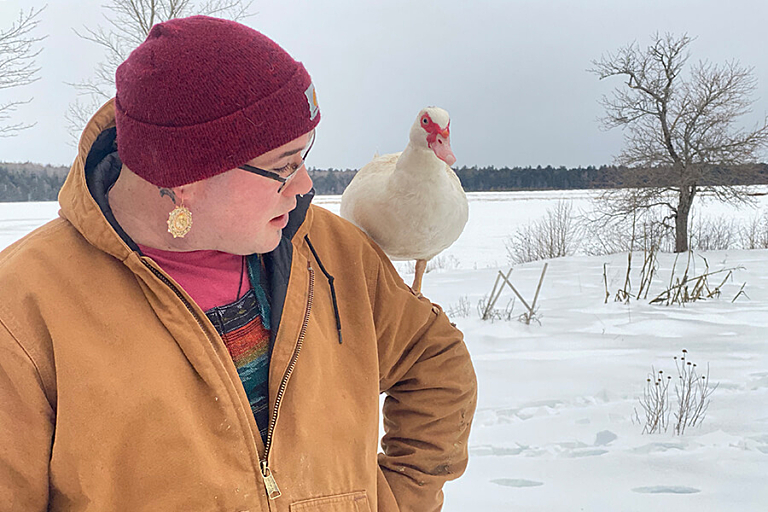 A person in a red hat stand outside in the snow with a duck on their shoulder