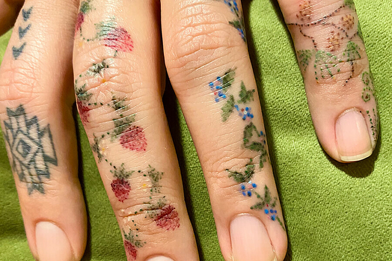 A close up photo of a persons hands with small flower and fruit tattoos