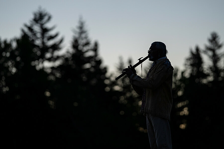 A silhouette of a forest and a man playing a flute during sunrise